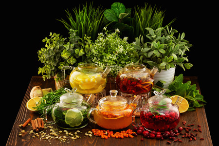Set of colorful glass tea pots decorated with green plants and berries on a wooden table board at dark background.の写真素材