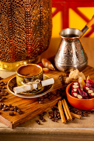 Cup of turkish black coffee on a plate at a wooden board at decorated table with candles, beans and sweets background.の写真素材
