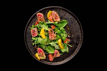 Top view plate of tuna salad served with arugula, spinach and white sesame seeds isolated at black background.の写真素材