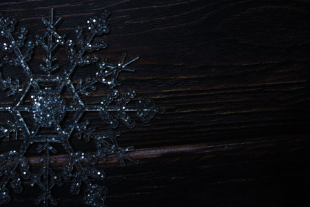 Silver glitter snowflake ornaments arranged on a dark rustic wooden background, creating a festive Christmas, cozy festive mood and winter holiday themeの写真素材