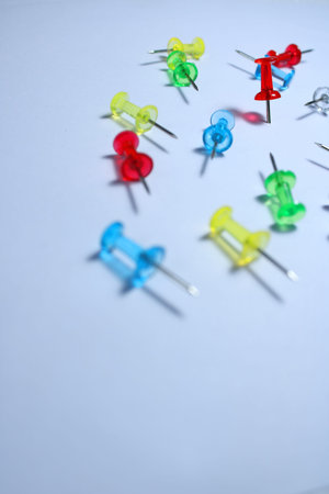 Colorful plastic push pins scattered on a white background, symbolizing organization, office work,...