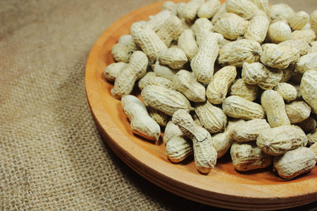 Raw peanuts in shell served in a wooden bowl on rustic burlap fabric. Natural food ingredient,...