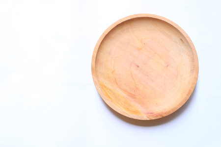Empty round wooden plate on white background. Minimalist top view mockup for organic food branding, natural kitchenware, and professional culinary layouts with copy spaceの写真素材