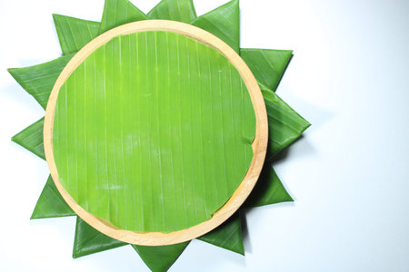 Top view of a wooden plate lined with a fresh green banana leaf and decorated with folded banana leaves in a star pattern. Ideal for food mockup and tropical menu backgroundの写真素材