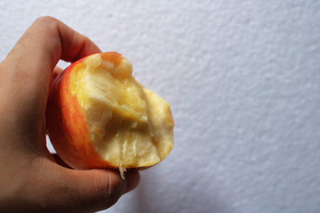 A close up of a hand holding a bitten apple against a clean white background. Fresh fruit, healthy eating, and natural lifestyle concept with copy spaceの写真素材