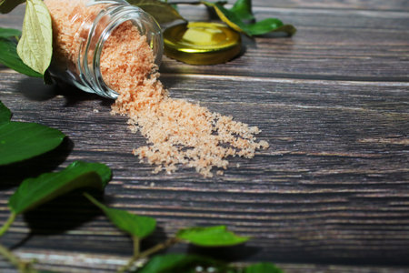 Himalayan Pink Salt Spilled from Glass Jar on Dark Wood Table with Green Leaves