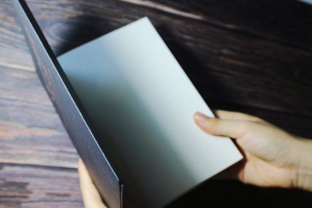 Close up of hand opening a blank sketchbook with empty white pages on dark wooden background....
