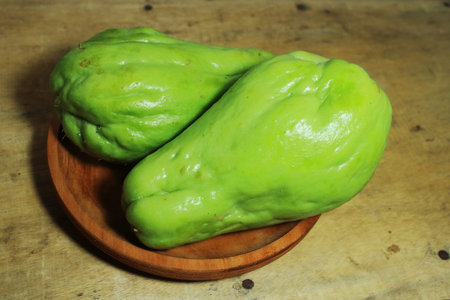 Fresh green chayote squash on a wooden plate over rustic table