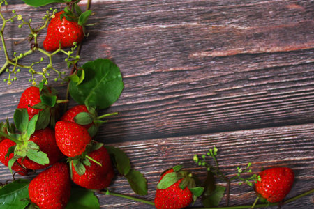 Red Strawberries with Green Leaves and Vines Clustered in The Corner of Dark, Rustic Wooden Backgroundの写真素材