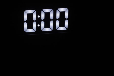 Minimalist Digital Clock Showing 0:00 Glowing in the Dark. Bright White LED Numbers on Black...