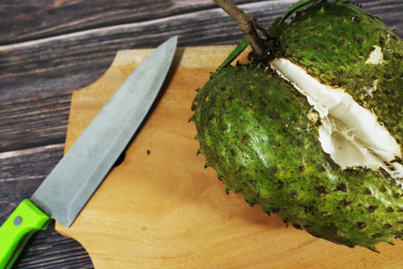 Fresh Soursop Fruit Being Cut on Wooden Board with Kitchen Knife