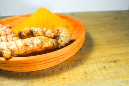 Fresh turmeric roots and ground turmeric powder on a wooden plate, showcasing natural spice used in cooking, herbal medicine, and healthy nutritionの写真素材