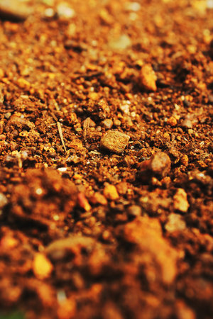 Close up of red soil texture with small stones, pebbles and rough ground surface. Natural earth background for geology, agriculture, construction and design use