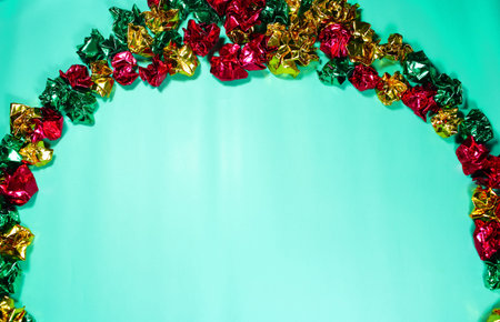 Flat lay border of crumpled metallic foil paper in red, green, and gold against a solid light teal background. Perfect copy space for Christmas and New Year promotions