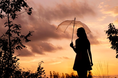 Silhouette of woman holding umbrella with sunset skyの写真素材