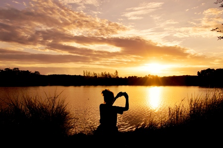 Silhouette of woman taking picture at the lakeの写真素材