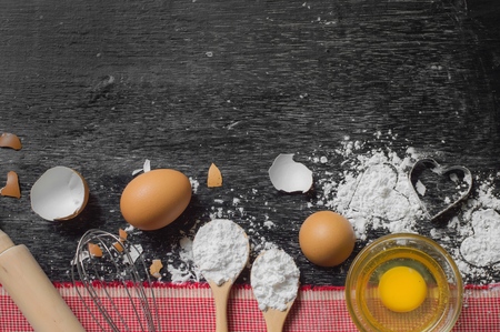 heart of flour, flour in wooden spoon, whisk, rolling pin and eggshell on wooden table for baking backgroundの写真素材