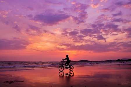 Silhouette of boy riding a bicycle on the beach with drametic skyの写真素材