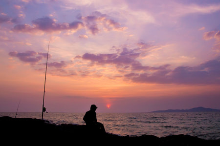 Silhouette of fisherman sitting on the stone at seasideの写真素材