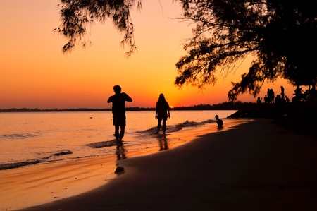 Silhouette of man taking picture his girlfriend on the beach at sunsetの写真素材