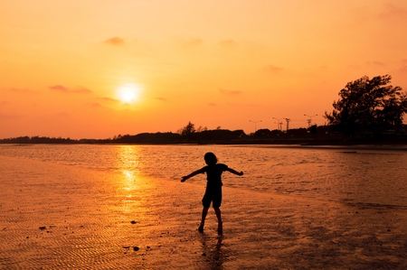 Silhouette of girl playing on the beach at sunsetの写真素材