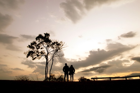 Silhouette of couple standing beside a tree on the hill at sunsetの写真素材