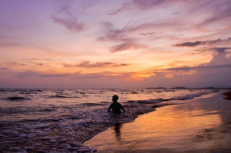 Silhouette of boy playing on the beach at sunsetの写真素材