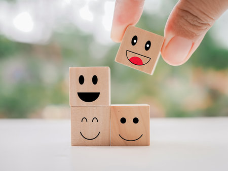 Close up hand holding happy face wooden block. Customer service rating experience, feedback emotion and satisfaction survey.の写真素材