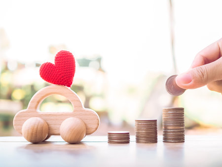Close up of hand putting coins in stack of coins and wooden toy car for transport and manage success business concept. Concept of car loanの写真素材