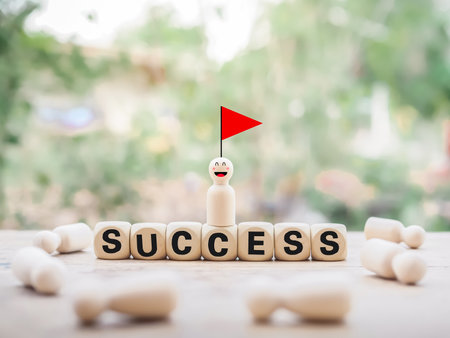 Wooden human figure on top of wooden block with the word SUCCESS and red flag. Human Resource Development concept. Goals achievement and business success.の写真素材