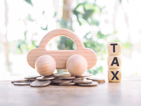 Wooden toy car on stack of coins and wooden blocks with the word TAX. The concept of paying tax for car.の写真素材