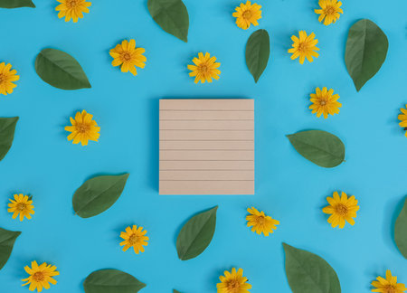 Directly above view of blank notebook with orange flower and green leaf on blue background.の写真素材
