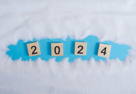 Wooden block with number 2024 and white sand on blue background. Top view with copy space of summer...