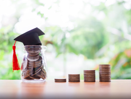 Glass bottle with graduation hat and stack of coins. The concept of saving money for education, student loan, scholarship, tuition fees in futureの写真素材