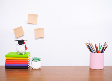 Office desk table, Student creative desktop with colorful stationery, hardcover book, sticky notes. Piggy bank with graduation hat, potted cactus. Copy space for text, Back to school, Education conceptの写真素材