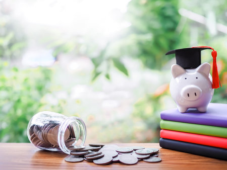 Piggy bank with graduation hat on colorful hardcover books, Glass bottle and stack of coins. The concept of saving money for education, student loan, scholarship, tuition fees in futureの写真素材