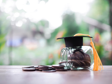 Glass bottle with graduation hat and stack of coins. The concept of saving money for education, student loan, scholarship, tuition fees in futureの写真素材