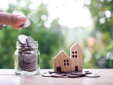 Close up hand putting coin into glass bottle and Miniature house on stack of coins. The concept of saving money for house, Property investment, House mortgage, Real estste.の写真素材