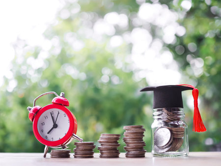 Glass bottle with graduation hat and red alarm on stack of coins. The concept of saving money for...