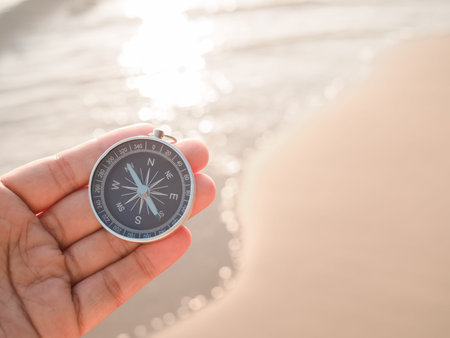 Close up hand holding compass with beach background