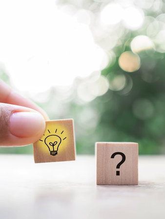 Close up hand arranging wooden block with light bulb and wooden block with question mark for...