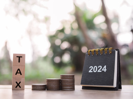 2024 desk calendar, Wooden block with word TAX and stack of coins. The concept of saving money for...