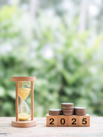 Hourglass, Wooden blocks with the number 2025 and stack of coins. The concept of saving money for...