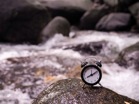 Black alarm clock on the rock with stream as background. The concept of world tourism day, Searching...