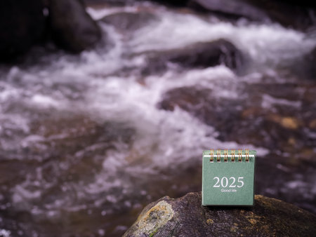 2025 desk calendar on the rock with waterfall as background. Resolution, Goal, Action, Planning, and...