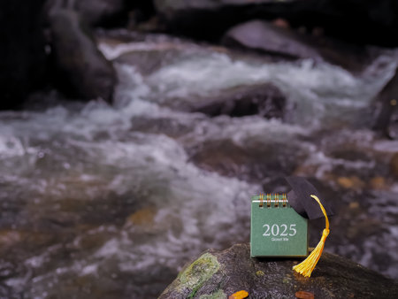 Study goals, 2025 Desk calendar with graduation hat on the rock with waterfall as background. The concept for Resolution, Goal, Action, Planning, and manage time to success graduate.の写真素材