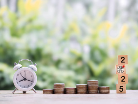 White alarm clock, Wooden blocks with the number 2025 and stack of coins. The concept of saving...