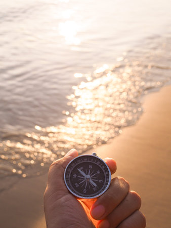 Close up hand holding compass with beach background in the sunset time