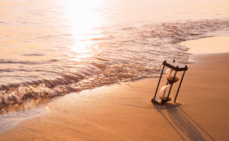 Hourglass on the beach in the sunset time. The concept about countdown to Summer, Travel, Vacation and Relaxation.の写真素材