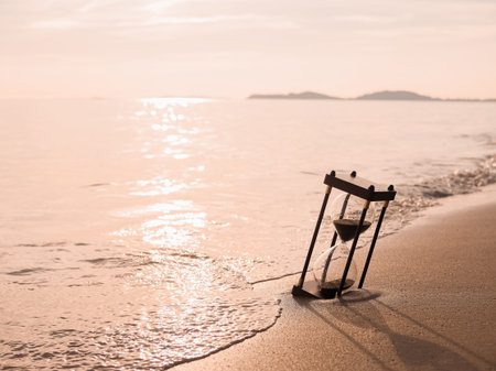 Hourglass on the beach in the sunset time. The concept about countdown to Summer, Travel, Vacation...